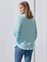 Blusa color celeste con escote en V, mangas largas acampanadas con detalle de crochet y frunces en los hombros.