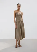 Vestido midi de corte evasé con estampado de cuadros vichy en tonos marrón y blanco. Presenta escote halter con tirantes finos para anudar al cuello, detalle fruncido en el centro del pecho y falda amplia de largo midi.
