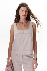 Top color beige claro con escote cuadrado y tirantes anchos. Presenta pespuntes decorativos en un tono más oscuro.