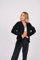 Conjunto de dos piezas confeccionado en tela plush, compuesto por una campera con cierre frontal y cuello alto, y un pantalón de corte recto. Presenta un diseño minimalista y cómodo en color gris claro.