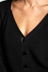 Cardigan negro de algodón con cuello en V, cierre frontal de botones y mangas largas con textura calada. Presenta puños y ruedo acanalados.