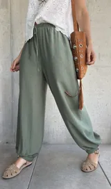 Pantalón tipo babucha de color verde militar, con cintura elástica fruncida y cordón ajustable. Cuenta con diseño amplio y puños elásticos en los tobillos.