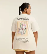 Remera de algodón color blanco, de corte holgado y alargado, con cuello redondo, manga corta y un delicado estampado floral con la frase "Flowers Bloom" en el lado izquierdo del pecho.