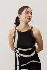 Vestido largo de punto con diseño geométrico y de ondas en color negro y crudo, sin mangas, con escote halter y detalle de flecos en el ruedo.