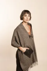 Chal de lana fina sin teñir con diseño de cuadros sutiles, cierre frontal con alamar y bolsillos de cuero metalizado. Presenta terminaciones con flecos en el ruedo y un calce estructurado en los hombros.
