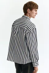 Camisa de popelina de algodón con diseño de rayas verticales en azul y blanco, cuello inglés, cierre frontal de botones y un bolsillo en el pecho. Presenta mangas largas con puños abotonados y corte relaxed fit.
