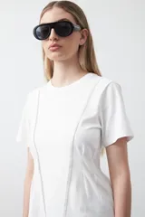 Remera de manga corta y cuello redondo, confeccionada en algodón. Presenta costuras verticales visibles en el frente que generan un efecto de entalle y estructura en la cintura.