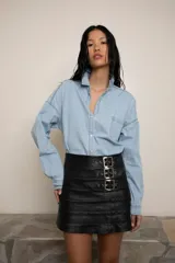 Minifalda de cuero negro con diseño de paneles horizontales y cierre lateral con tres hebillas metálicas decorativas en el frente.