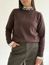 Sweater de punto color beige, con cuello redondo adornado con apliques de pedrería y detalle de puntilla blanca en el cuello y los puños.