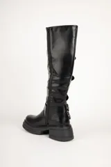 Bota de caña alta color negro, con suela track y múltiples hebillas metálicas.