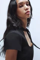Vestido corto negro de cuello redondo con lazada, escote cuadrado y manga corta, con cierre en la espalda con cremallera oculta.