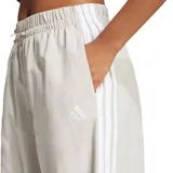 Pantalon Adidas de mujer, de corte ancho y estilo deportivo, color beige con las icónicas tres tiras blancas laterales y logo de la marca bordado.