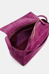 Mini bolso de mano confeccionado en piel de gamuza color fucsia. Presenta un diseño estructurado con asa corta, cierre principal mediante cremallera y solapa, y bolsillos exteriores en la parte frontal y trasera.