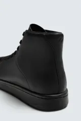 Zapatilla tipo botín de estilo minimalista fabricada en piel lisa de color negro. Presenta un diseño de caña media con cierre de cordones al tono y suela plana de goma a juego.