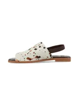 Sandalia plana Isotta de cuero con pelo, con estampado animal print tipo vaca en tonos blanco, marrón y negro. Cuenta con elástico trasero marrón y suela plana.
