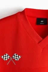 Remera de malla color rojo, con cuello en V, mangas cortas y corte oversized. Cuenta con diseño estampado frontal de Honda con banderas a cuadros y el logo de la marca.