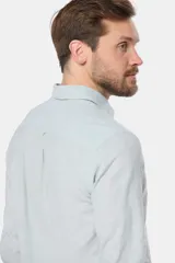 Camisa de manga larga, corte slim fit, color celeste con finas rayas verticales blancas. Presenta cuello camisero y un pequeño logo bordado en el pecho.