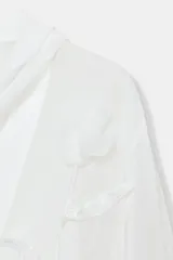 Blusa de tejido semitransparente con efecto arrugado, escote en pico y manga larga. Presenta un detalle decorativo frontal con estructura en forma de flor.