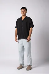 Camisa de manga corta color negro, con cuello cubano y botones frontales. Tejido de lino con textura entramada.