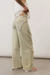 Pantalón de jean de corte wide leg, tiro medio y lavado claro con efecto desgastado. Presenta diseño de múltiples paneles con costuras pespunteadas verticales y roturas en ambas piernas.