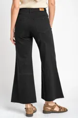 Jean de corte wide leg y tiro medio, confeccionado en algodón peinado de color negro. Presenta un diseño de pierna ancha con ruedo deshilachado y cierre frontal con botón y cremallera.