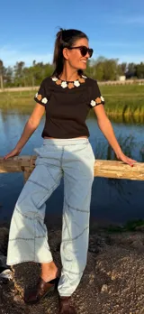 Remera negra de algodón con cuello redondo y mangas cortas. Presenta flores de crochet en tonos beige y blanco en el contorno del cuello y las mangas.