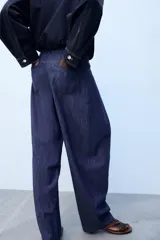 Pantalón confeccionado con lino de tiro alto con pliegues delanteros y cinco bolsillos. Presenta pernera holgada y cierre frontal con cremallera, botón interior y gancho.