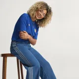 Pantalón Adidas Firebird de denim azul de corte holgado, con tiro medio y las icónicas tres tiras blancas a lo largo de los laterales de las piernas.