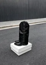 Botas de caña alta negras con punta en pico, taco bajo y detalles metálicos plateados en los laterales de la caña.