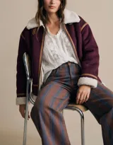 Campera tipo gamulán de corte oversize, color bordó con interior y cuello de corderito sintético en color crema. Presenta detalles de ribetes en cuero sintético marrón y cierre frontal.