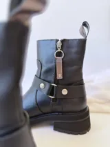 Bota corta negra de cuero, con caña media, hebilla lateral y suela track.