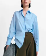 Camisa celeste de manga larga con diseño de rayas finas, cuello clásico, cierre frontal con botones y un bolsillo aplicado en el pecho.
