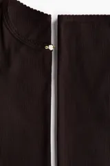 Pijama de dos piezas en punto acanalado color marrón oscuro. Incluye remera de manga larga con cuello redondo y detalle de aplique floral en el centro, y pantalón largo de corte recto con cintura elástica.