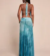 Vestido largo de tela vaporosa con estampado tie-dye en tonos azules y blancos. Presenta un escote halter con drapeado pronunciado y aberturas laterales en la cintura.