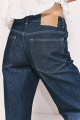 Pantalón jean de tiro alto, color azul oscuro, con corte holgado y pierna recta. Tiene cinco bolsillos y cierre con botón.