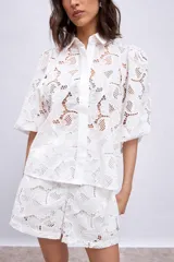 Camisa blanca de broderie con cuello clásico, mangas abullonadas 3/4 y cierre frontal con botones.