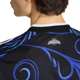 Camiseta de fútbol Adidas de la Selección Argentina, modelo visitante. Diseño en color negro con estampado de patrones florales y ornamentales en tonos azules, cuello redondo blanco y detalles de las tres tiras en los hombros. Incluye el escudo de la AFA, el logo de Adidas y el parche de campeón del mundo FIFA 2022.