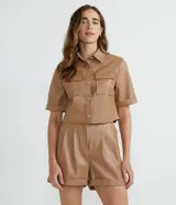 Camisa de manga corta confeccionada en cuero sintético color tostado, con cuello camisero, cierre frontal con botones en forma de corazón y dos bolsillos con solapa en el pecho.