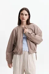 Campera verde militar sin cuello, con elástico y cinto regulable en la cintura, bolsillos amplios y cierre frontal.