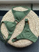 Bikini verde militar de tela acanalada. El top es de triángulos fijos unidos por una argolla, con breteles regulables y lazo en la espalda. El bottom es vedetina con argollas en la cadera.