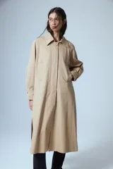 Trench midi de color camel, confeccionado en una mezcla de algodón y nylon con propiedades repelentes al agua. Presenta un diseño clásico con cuello camisero, cierre frontal de botones, bolsillos laterales y tajos en los costados.