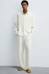 Pantalón de corte relajado confeccionado en tejido de cáñamo color blanco roto. Presenta cintura elástica con cordón interior ajustable, cierre frontal con botones, bolsillos laterales y un bolsillo trasero de plastrón.