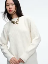 Sweater de tejido de punto acanalado en color blanco, con cuello redondo, mangas largas y corte holgado. Presenta un diseño minimalista y contemporáneo.