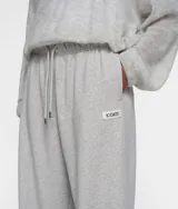 Pantalón de jogging gris de corte recto y estilo oversize, confeccionado en felpa de algodón. Presenta cintura elástica con cordón, bolsillos laterales y traseros, etiqueta con logo y puños elásticos en los tobillos.