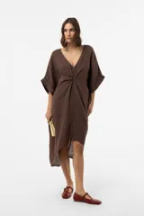 Vestido midi de lino color marrón, de corte amplio y silueta asimétrica con escote en V y detalle fruncido en el centro del frente. Presenta mangas cortas holgadas con vuelta y diseño relajado.