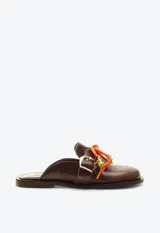 Zueco mocasín de cuero marrón, con taco plano, hebilla metálica dorada lateral y detalle de cordón naranja con cuentas decorativas en el empeine.