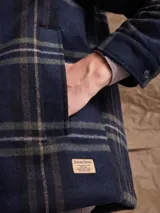 Chaqueta de lana con cierre frontal completo, diseño a cuadros en tonos azul marino y verde, cuello camisero y bolsillos laterales.