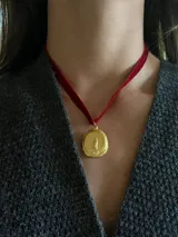 Gargantilla de terciopelo rojo con medalla circular dorada bañada en oro 18k, que presenta un diseño de la Virgen con acabado orgánico y textura artesanal.