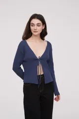 Saco de punto acanalado color azul, con escote profundo en V y cierre frontal mediante lazo para anudar. Presenta mangas largas y diseño holgado.