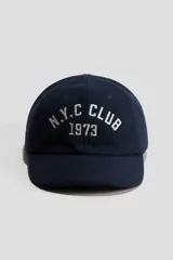 Gorra azul marino de sarga de algodón, con diseño bordado frontal con el texto "N.Y.C. CLUB 1973" en color blanco.